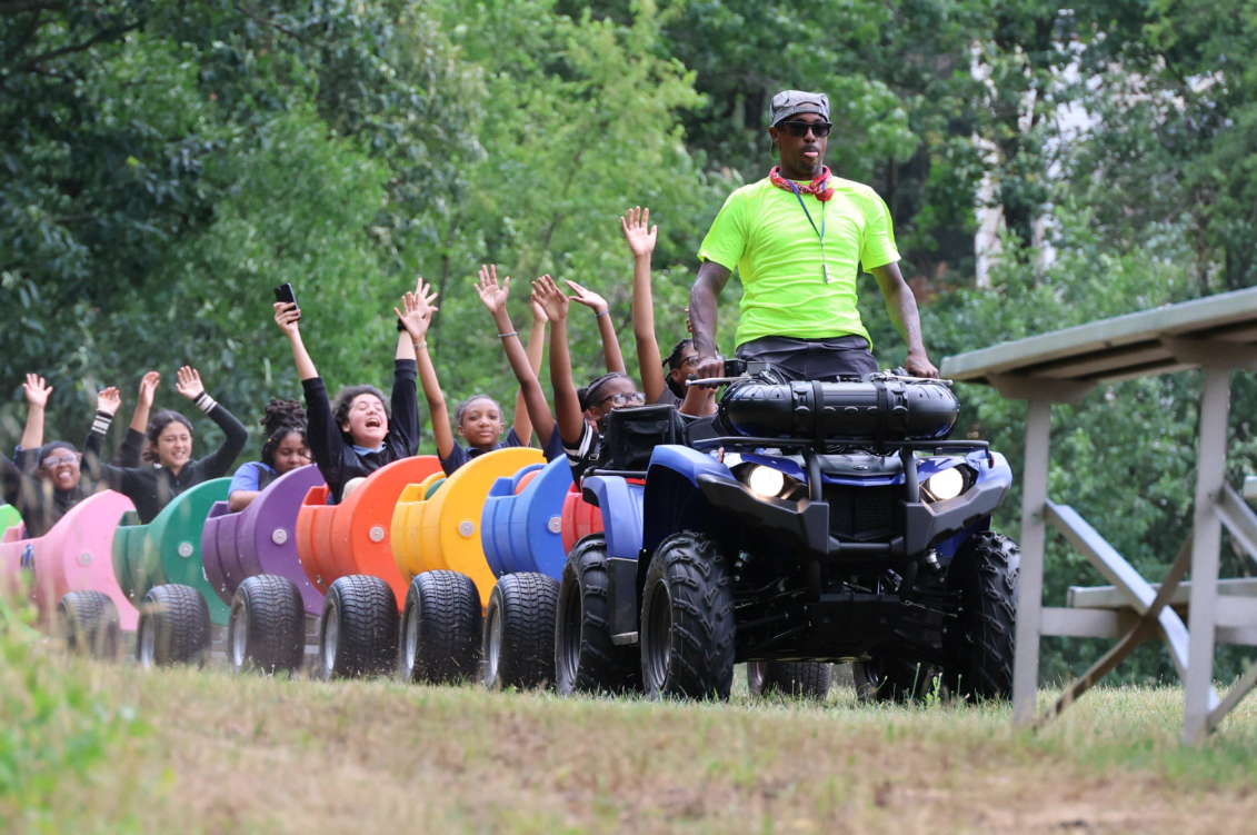 Kids with hands raised riding the colorful trackless train